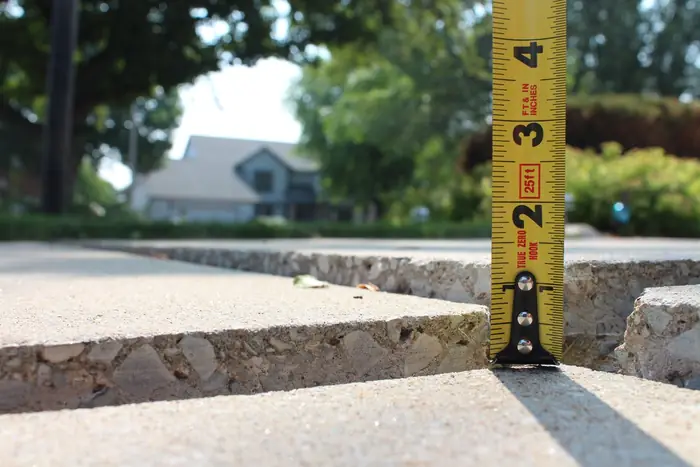 Tape measure showing a raised trip lip between sunken driveway slabs before polyurethane foam lifting