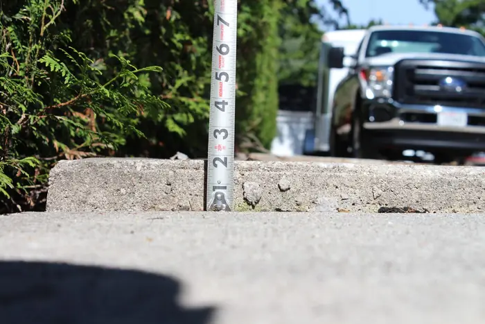Public sidewalk slab settled into a raised trip lip, measured with a tape, before polyfoam lifting