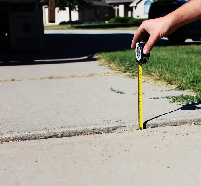 Sidewalk slabs settled into a broken seam, measured with a tape, before polyfoam lifting